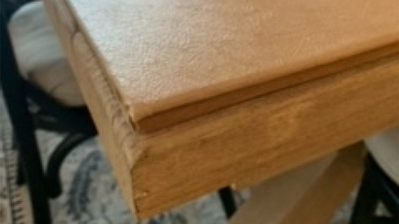 Closeup of the corner of an light oak table with a table pad on top.